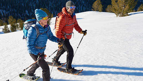 A couple outfitted with L.L.Bean snowshoes, poles and backpacks learning how to snowshoe on a snowshoe adventure.